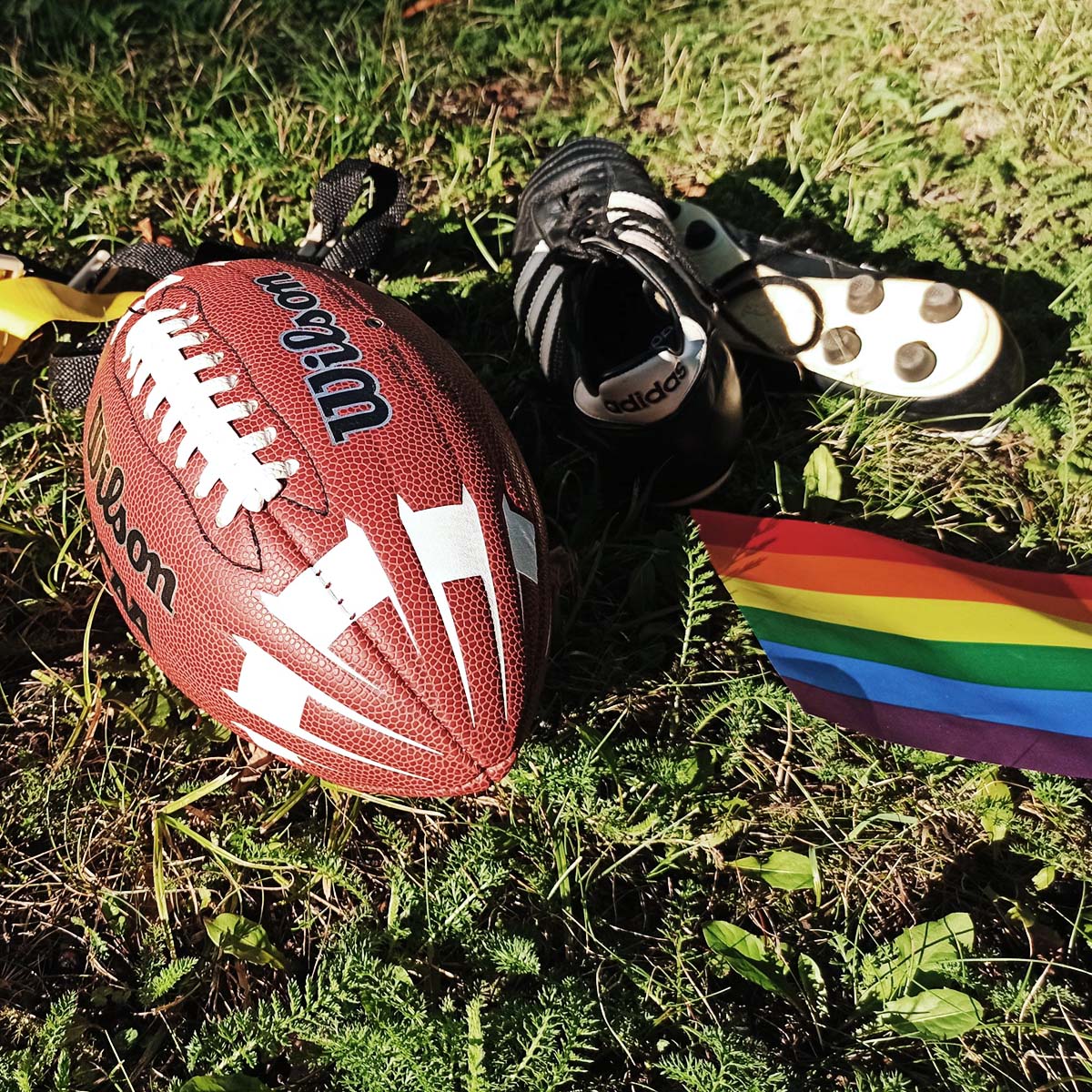 Ein Fußball, eine Regenbogenflagge und ein Paar Schuhe, die für Vielfalt und Gemeinschaft im Flag Football stehen.