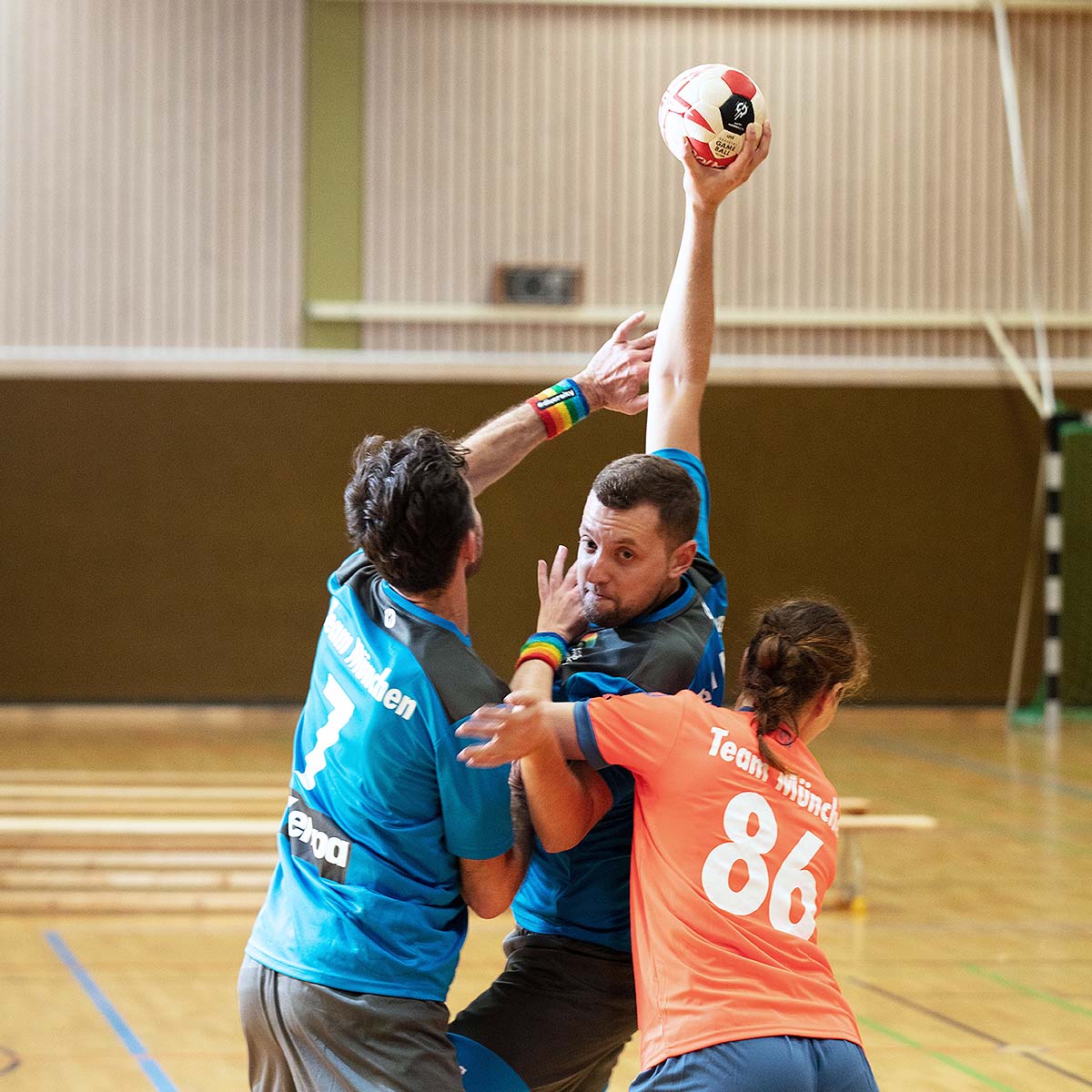 Drei Personen spielen Handball auf einem Spielfeld, voller Energie und Teamgeist.