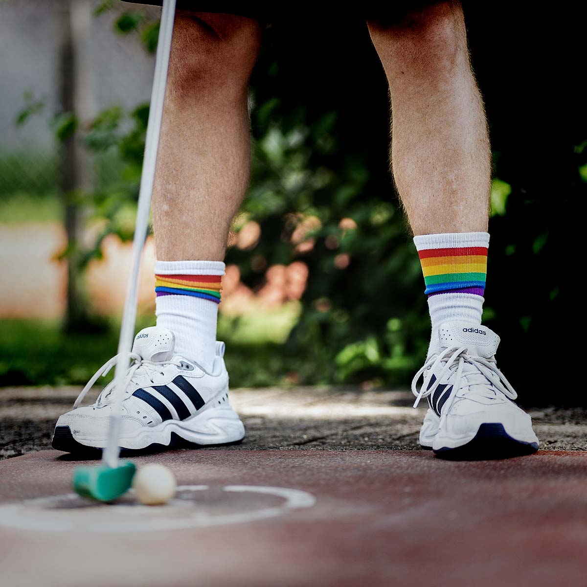 Eine Person mit Regenbogensocken steht mit einem Schläger und Ball in der Hand, bereit für Minigolf.