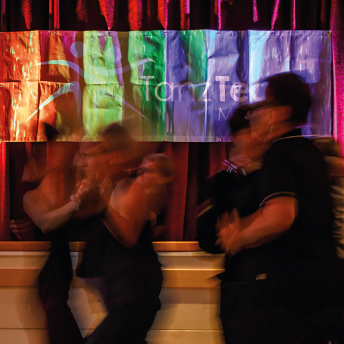 Mehrere Personen tanzen miteinander in farbigem Licht.