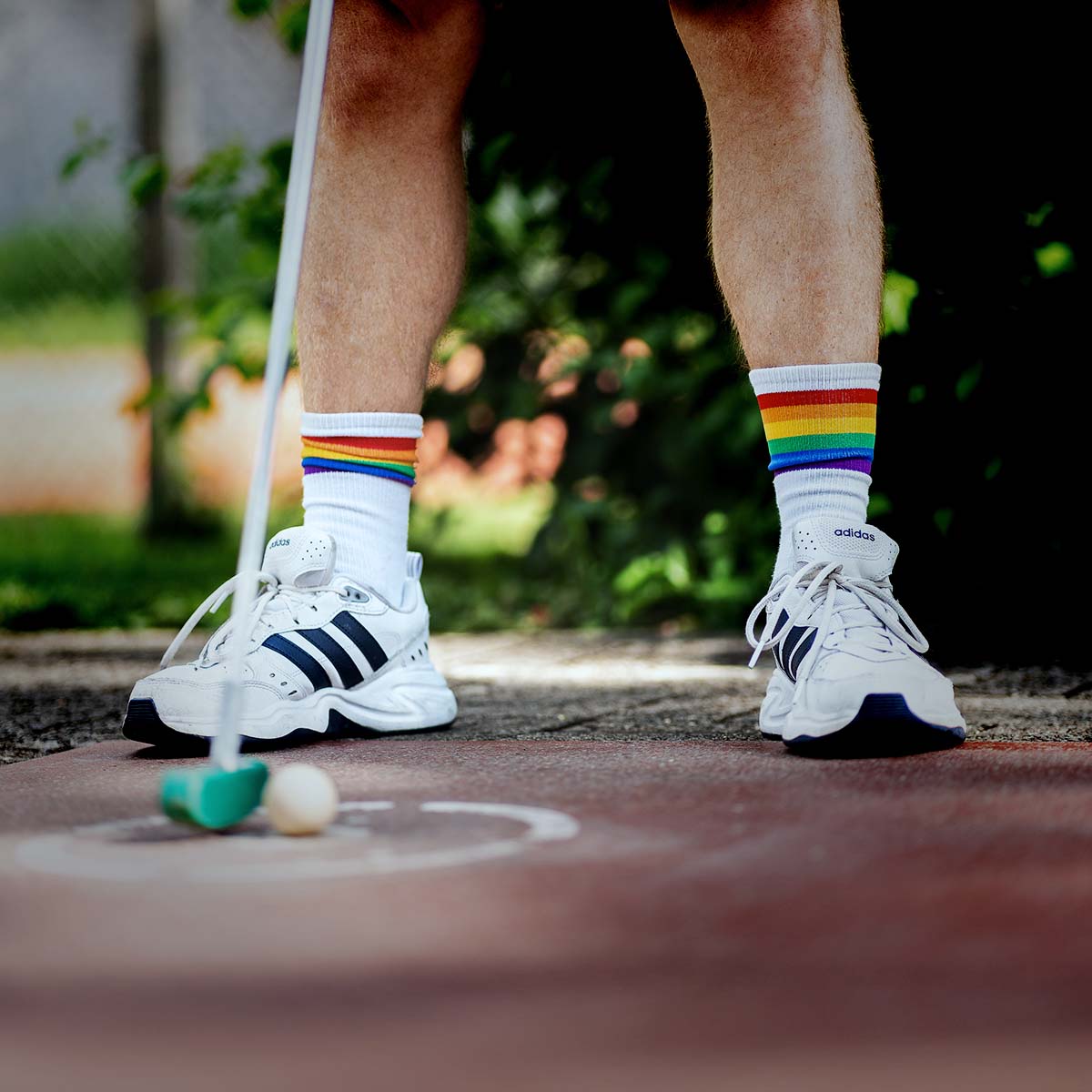 Ein Mann mit Regenbogensocken hält einen Golfball in der Hand.