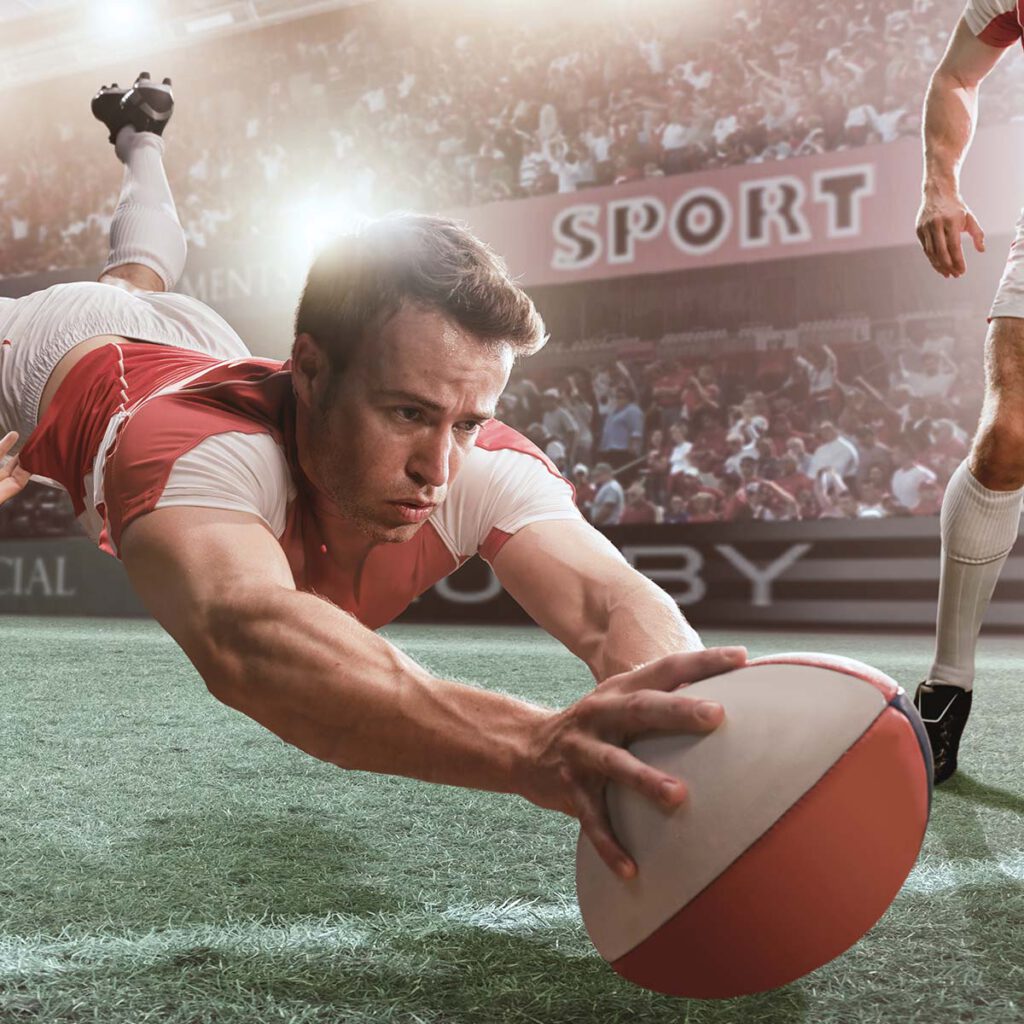 Rugby player jumps for the ball and stretches out on the grass.