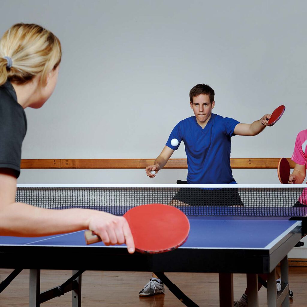 Several people are enthusiastically playing table tennis in a bright room.