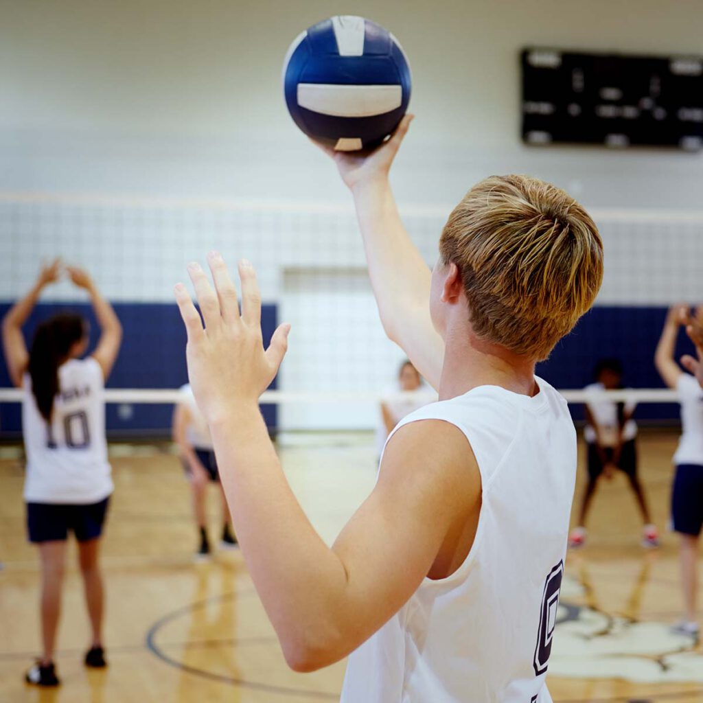 A young man is holding a volleyball in a sports hall.